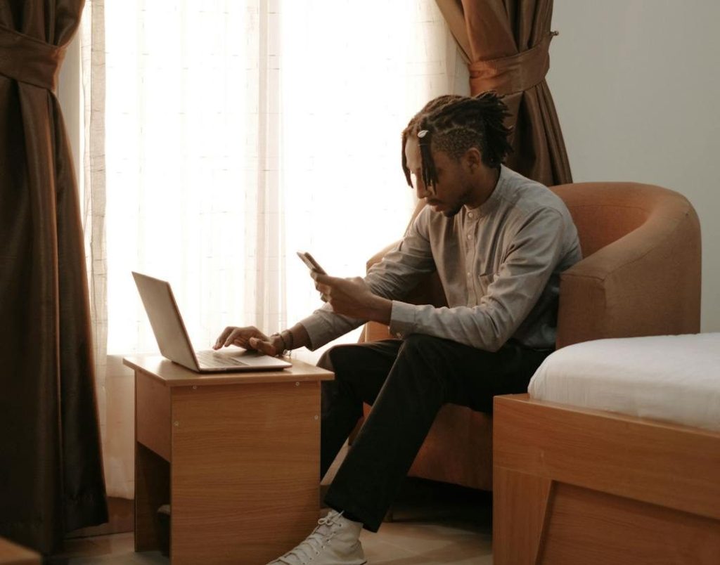 man sitting in an armchair working on a laptop and smartphone